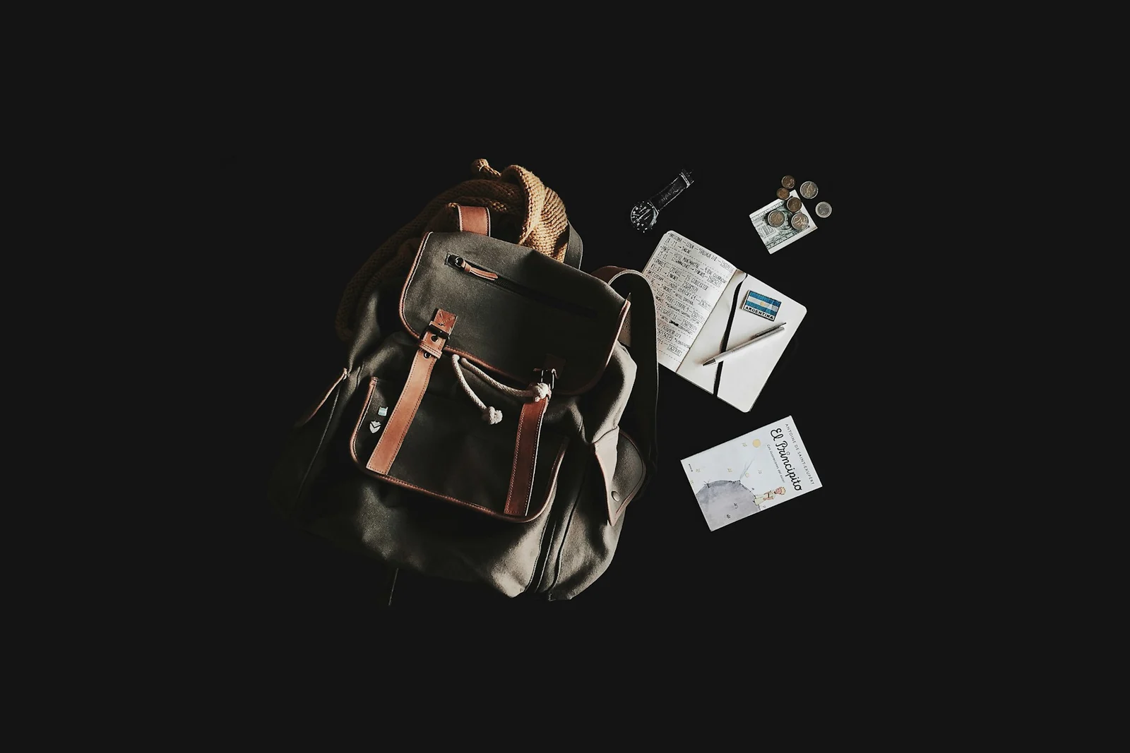 Petit sac à dos et accessoires de voyage disposés à plat sur un fond sombre