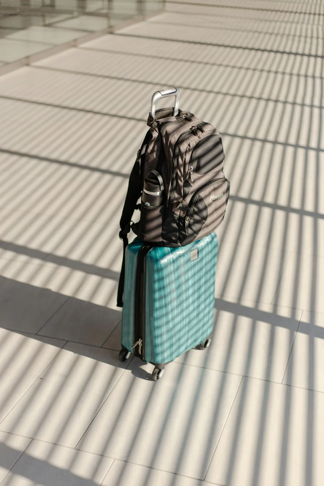 Un sac à dos à motifs posé sur une valise turquoise à roulettes.