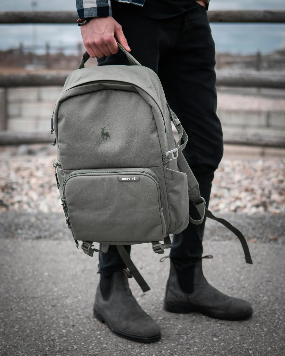 Sac à dos de voyage gris tenu par sa poignée, avec ses poches visibles